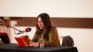 Deborah Feldman sitzt lesend vor einem Mikrofon an einem Tisch. © Nerea Lakuntza Foto: Nerea Lakuntza