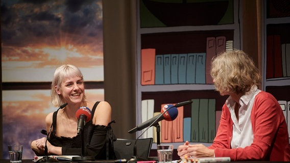 Helene Bukowski und Katja Weise sitzen an einem Tisch auf einer Bühne. © Marco Bühl Foto: Marco Bühl
