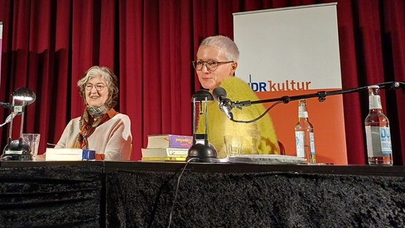 Barbara Kingsolver und Alexandra Friedrich sitzen an einem Tisch auf einer Bühne. © NDR Foto: Alexander Solloch