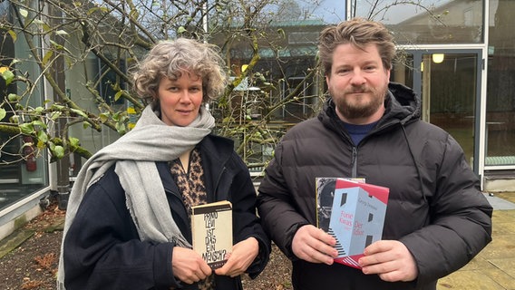Lisa Kreißler und Alexander Solloch stehen mit Büchern in der Hand auf einem Innenhof und schauen in die Kamera. © NDR Foto: Julia Beyer