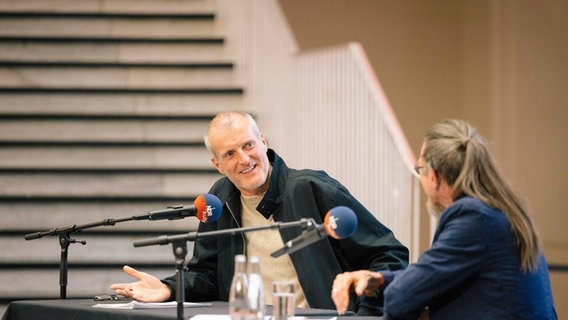 Robert Seethaler sitzt auf einer Bühne und sieht zu dem Moderator Joachim Dicks. © Nerea Lakuntza Foto: Nerea Lakuntza