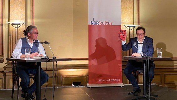 Steffen Kopetzky und Ulrich Kühn sitzen an Tischen auf einer Bühne. © Literaturhaus Hamburg 