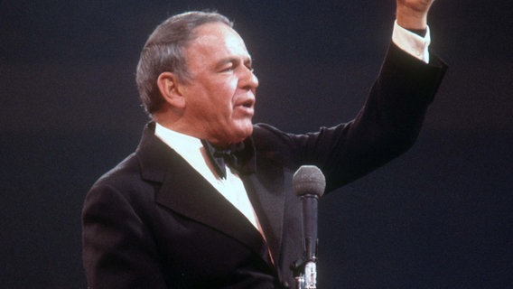 Der Sänger Frank Sinatra 1974 auf der Bühne mit einem Mikrofon. © picture alliance /Newscom 