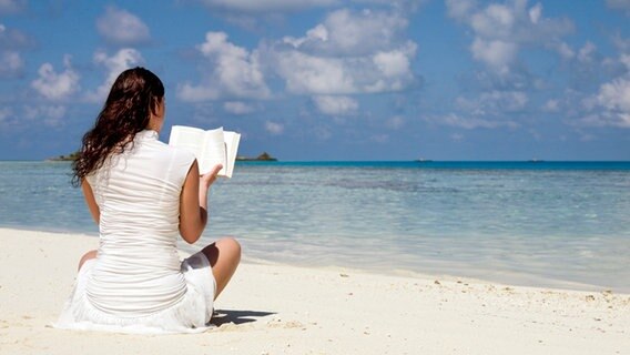Eine Frau liest am Strand in einem Buch. © iStock Foto: IvanovaInga