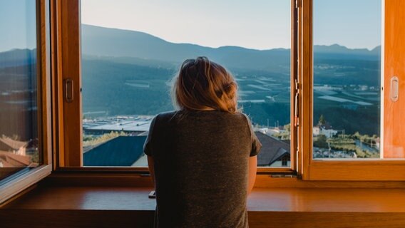 Eine junge Frau schaut aus dem Fenster auf eine Berglandschaft. © Z2sam / photocase.de Foto: Z2sam