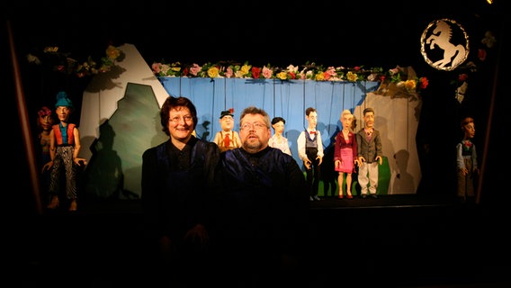 Silke Technau und Stephan Schlafke stehen vor einer Bühne mit Theaterfiguren © Stephan Schlafke / Kobalt Figurentheater Lübeck 