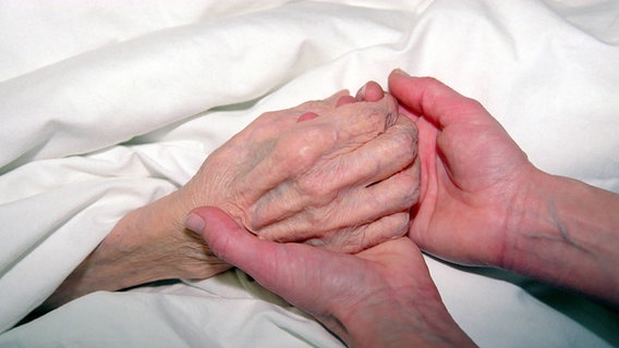 A woman holding the hand of a dying man © IMAGO / Lem 