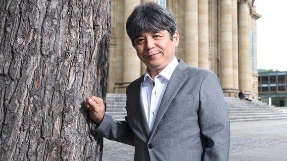 Der Komponist Toshio Hosokawa steht an einem Baum und blickt in die Kamera. © dpa Foto: Bernd Weissbrod