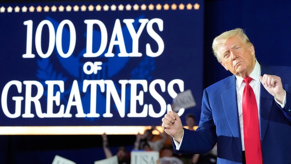 Donald Trump hat die Augen geschlossen und scheint vor einen Schild, auf dem "100 Days of Greantness" steht, zu tanzen. © Alex Brandon/AP/dpa +++ dpa-Bildfunk +++ 