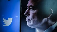 Das Gesicht von Elon Musk ist auf einem Handy zu sehen. Links daneben das Twitter-Logo. © picture alliance / ZUMAPRESS.com Foto: Adrien Fillon