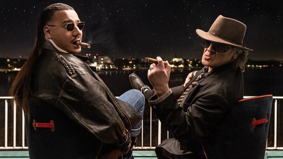 Udo Lindenberg und Apache 207 rauchen eine Zigarre auf einem Balkon. © picture alliance/dpa/Warner Music | Tine Acke 