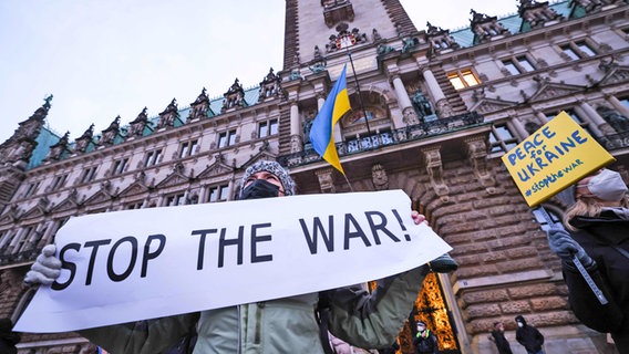 Menschen vor dem Hamburger Rathaus bei einer Kundgebung halten Schilder mit "Hentikan perang" wegen des Krieges in der Ukraina hoch © Christian Charisius/dpa +++ dpa-Bildfunk +++ Foto: Christian Charisius