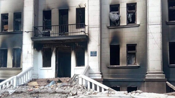 Die Vorderansicht des Theaters von Mariupol in der Ukraine. Es gibt keine Glasfenster mehr und über den Fenstern sind schwarze Brandflecken. © picture alliance/dpa/Azov Battalion/AP | Uncredited Foto: Azov Battalion/AP | Uncredited