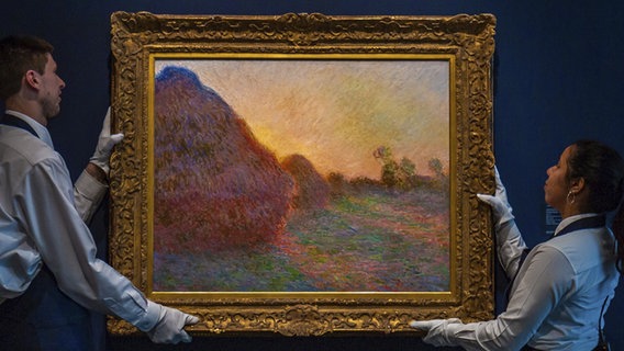 Zwei Mitarbeiter von Sotheby's tragen das Monet-Bild "Meules". © picture alliance/Uncredited/Sotheby's/AP/dpa 