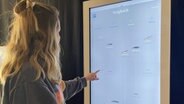 A young woman poses in front of an interactive screen comparing various marine organisms © NDR Photo: Frank Hajasch
