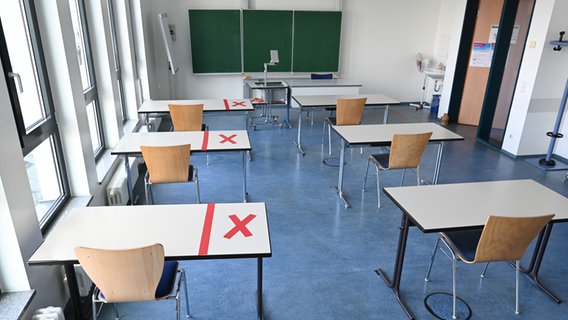 Mit einem aufgeklebten roten "X" ist ein Teil von Tischen in einem leeren Raum einer Volkshochschule (VHS) markiert, damit die Kursteilnehmer Abstand zueinander halten. © picture alliance/dpa Foto: Arne Dedert