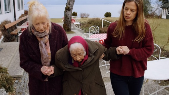 Zwei Frauen stützen eine ältere Frau beim Gehen. © FlareFilm 