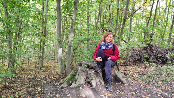 Eine Frau sitzt in einem Wald auf einem Baumstumpf. © NDR / Svenja Estner 