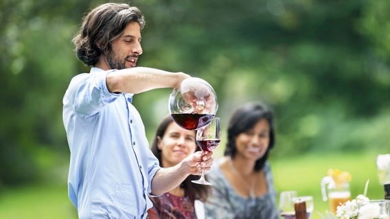 Ein Mann gießt auf einer Gartenparty Wein in ein Glas © imago 