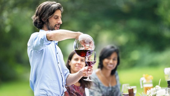 Ein Mann gießt auf einer Gartenparty Wein in ein Glas © imago 