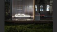 Aus einer weißen Neonröhre ist der Umriss einer obdachlosen Person geformt, die im Dunkeln auf einer Bank liegt. © Jakob Bahret 