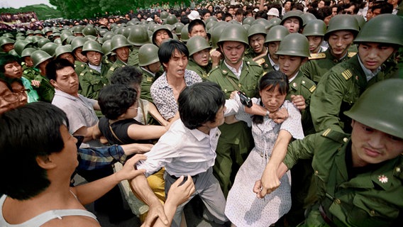 Eine junge Frau wird von Soldaten festgehalten, ein Mann in Zivil drückt den Arm auf ihren Hals. © Jeff Widener/AP Foto: Jeff Widener