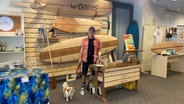 Der Surfboard-Bauer Rudi von "Woody's Surfboards" steht in dem Lübecker Pop-up-Store "Feines aus Lübeck" vor einigen seiner Holz-Boards. © Inessa Baur/NDR 
