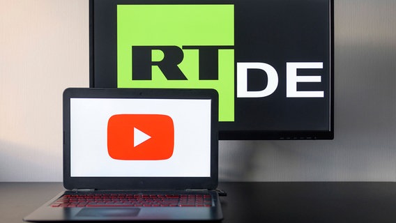 Fotomontage: Ein Fernseher mit dem Logo des Senders RT DE, davor ein Notebook mit dem YouTube-Logo © imago 
