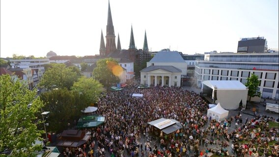 Ein großer Platz auf dem hunderte Menschen vor einer Bühne stehen, im Hintergrund sieht man Kirchtürme. © Kultursommer Oldenburg 