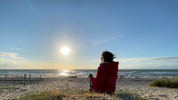 Heike Götz sitzt im Sonnenschein am Strand von Fehmarn. © NDR Foto: Sebastian Dubielzig