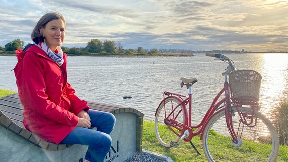 Heike Götz sitzt auf einer Bank am Wasser. Das Landpartie-Fahrrad steht daneben. © NDR Foto: Sebastian Dubielzig