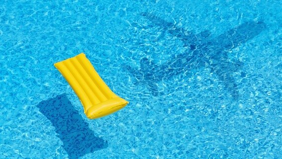 Eine gelbe Luftmatratze schwimmt in einem Pool mit blauem Wasser,  in dem der Schatten eines Flugzeuges zu sehen ist. © Photocase Foto: SRNR
