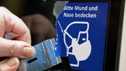 Ein Piktogramm mit dem Hinweis auf die Maskenpflicht wird mit einem Schaber entfernt © Picture Alliance Foto: Bernd Wüstneck