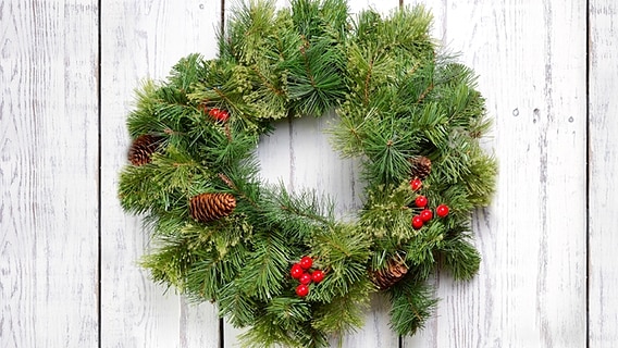 Ein Adventskranz hängt an einer weißen Holzwand. © iStock Foto: Ivan Fisun