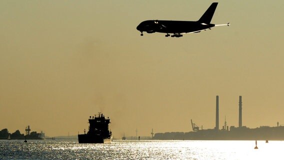 Ein Airbus A380 fliegt in Hamburg über die Elbe vor Blankenese im Gegenlicht, um auf dem Werksflughafen in Finkenwerder zu landen. © dpa Foto: Maurizio Gambarini