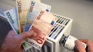Hand mit Geldscheinen vor einem Heizkörper © picture-alliance 