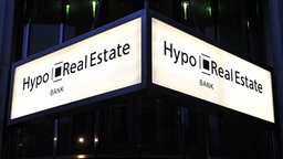 An einer Bankfiliale der Hypo Real Estate in Berlin leuchtet das Eingangsschild des Unternehmens. © dpa / picture-alliance 