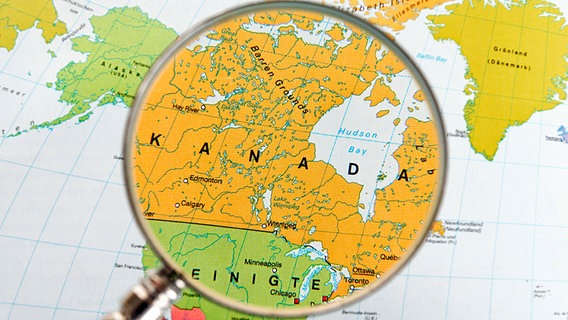 Eine Lupe vergrößert Kanada und den Norden der USA auf einer Landkarte © picture-alliance/chromorange Foto: Ralph Kerpa