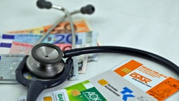 Geldscheine, Stethoskop und Krankenversicherungkarten liegen auf einem Tisch © dpa 