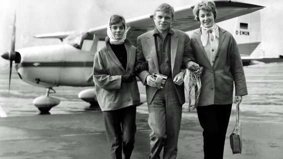 Von links: Renate Densow, Hardy Krüger, Christiane Krüger bei ihrer Ankunft am Flughafen Surrey in England. © dpa / picture alliance Foto: UPI
