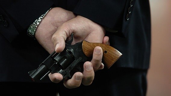 Ein Mann hält eine Schusswaffe hinter seinem Rücken © picture-alliance / Sven Simon Foto: SVEN SIMON