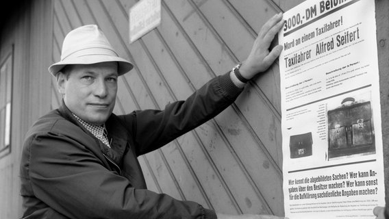 Regisseur Jürgen Roland bei den Dreharbeiten zu der Stahlnetz-Folge "Nacht zum Ostersonntag": Er hält ein Plakat an eine Holzwand. © NDR 