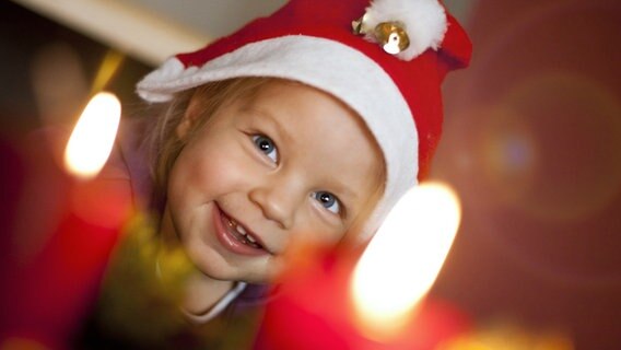 Ein kleines Kind mit Weihnachtsmütze sitzt vor einem Adventkranz mit brennenden Kerzen. © picture alliance/EXPA/APA/picturedesk.com 