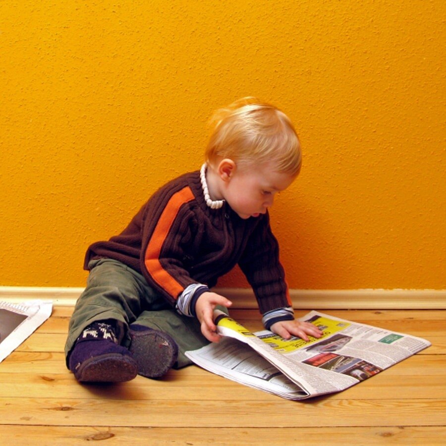 Kleinkind sitzt auf dem Boden und 'liest' Zeitung. © panthermedia.net 