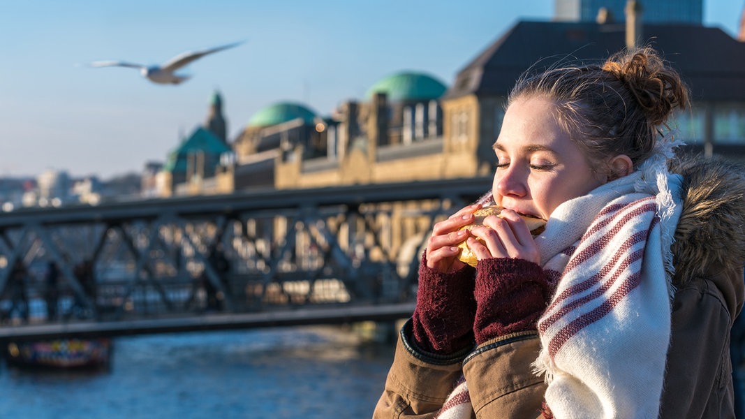 Eine Frau isst ein Brötchen im Hamburger Hafen.
