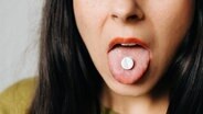 Eine Frau streckt ihre Zunge heraus, auf der eine Tablette liegt. © Photocase Foto: Eliza