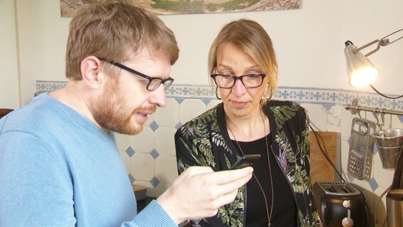 Die Wissenschafts-Journalisten Hinnerk Feldwisch-Drentrup und Nicola Kuhr sind in einer Küche und lesen auf dem Handy eine Nachricht. © NDR Foto: Screenshot