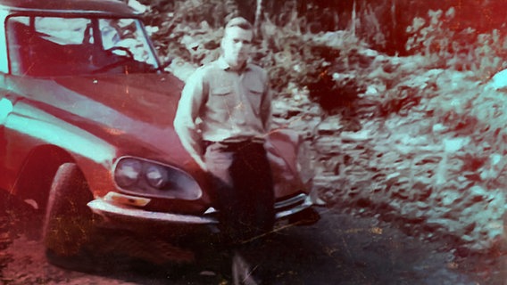 Historisches Schwarz-Weiß-Bild von Wichmann, der in Hemd und Hose auf dem Kühler seines Autos lehnt. © NDR/Studio Fritz Gnad 