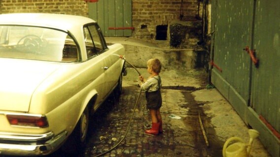 Ein kleiner Junge steht mit einem Wasserschlauch vor einem Auto. © photocase Foto: Mr.Nico