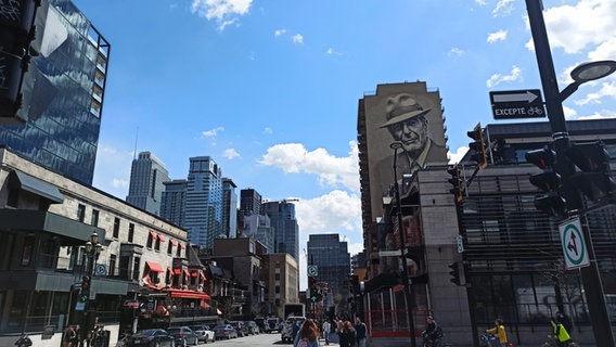 Zu sehen sind viele hohe Gebäude in der Stadt Montréal, auf einer Fassade ist ein Gesicht von Musiker Leonard Cohen gezeichnet worden in schwarz, weiß. © Eva Schramm / NDR Foto: Eva Schramm